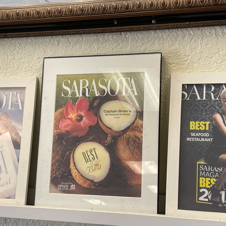 Framed Sarasota Magazine cover featuring coconuts, a hibiscus, and "Captain Brian's Best Restaurant for Seafood" text.