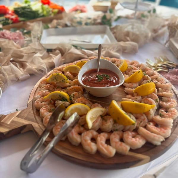 A wooden platter of Captain Brian's shrimp cocktail with lemon wedges and cocktail sauce.
