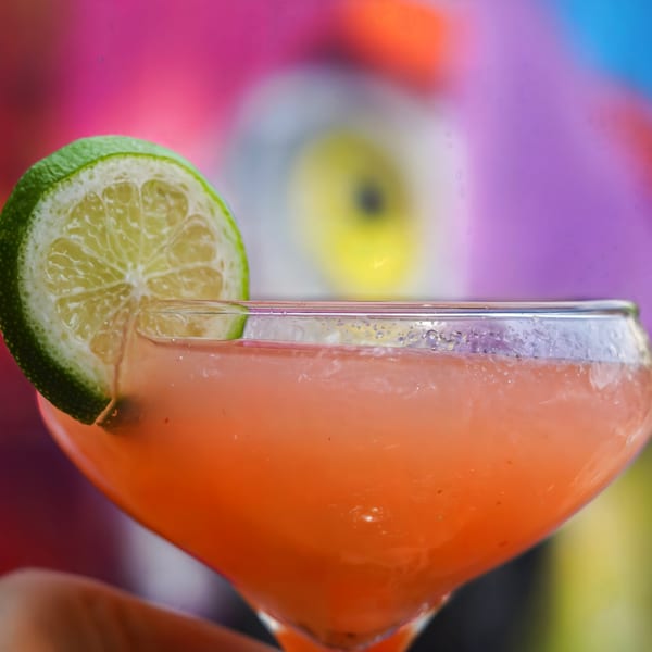 Close-up of a pink cocktail garnished with a lime slice against a colorful, blurred background.