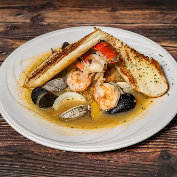 Captain Brian's seafood stew with shrimp, lobster, mussels, clams, and toasted bread on a white plate.
