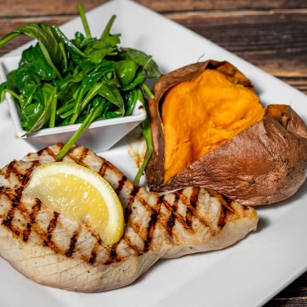 Grilled fish with a lemon slice, a baked sweet potato, and a side of green spinach.