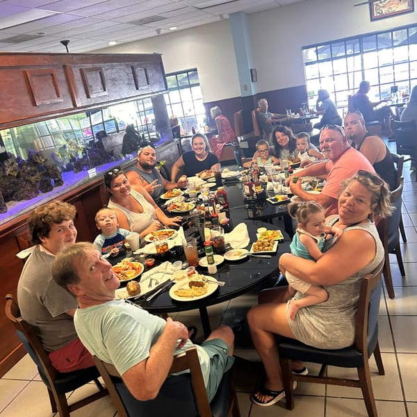 A large family group enjoys a meal at Captain Brian's Seafood Market & Restaurant, with an aquarium nearby.