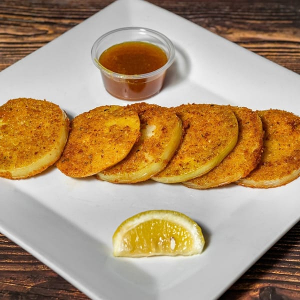 Fried green tomatoes with a side of dipping sauce and a lemon wedge on a white plate.