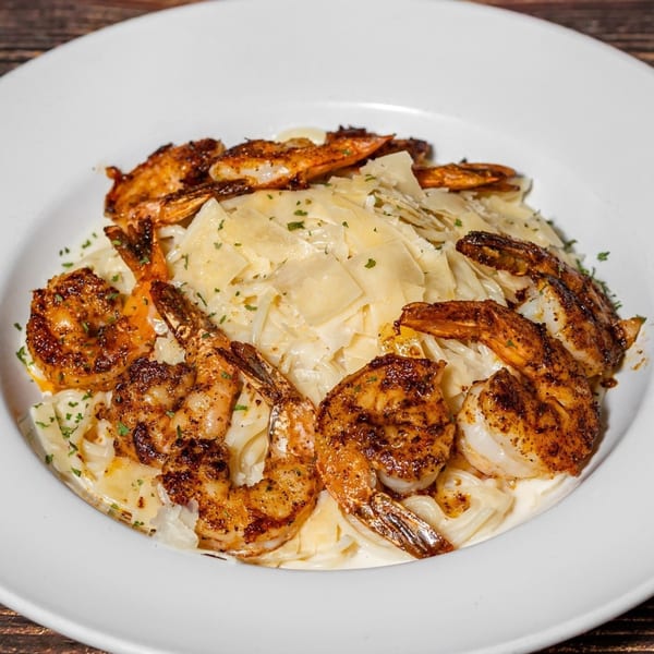 Captain Brian's blackened shrimp pasta with shaved Parmesan and parsley in a white bowl.