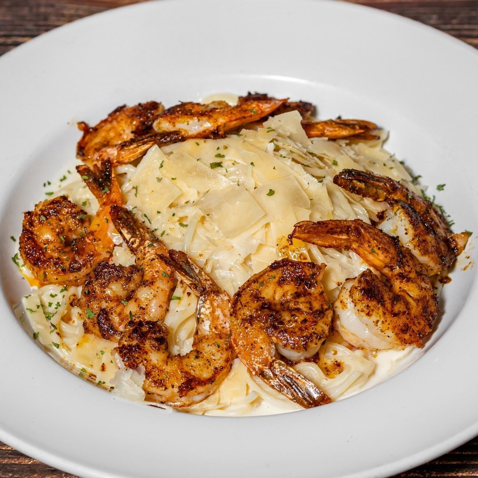 Captain Brian's blackened shrimp pasta with shaved Parmesan and parsley in a white bowl.