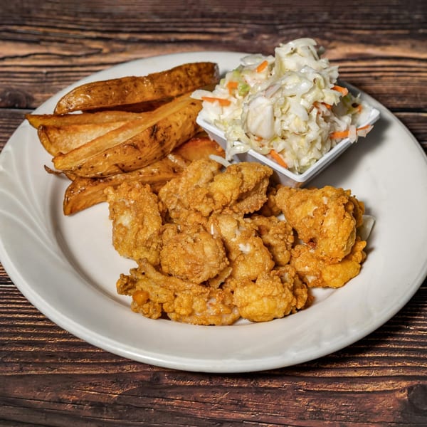 Fried seafood platter with crispy potato wedges and a side of creamy coleslaw on a white plate.